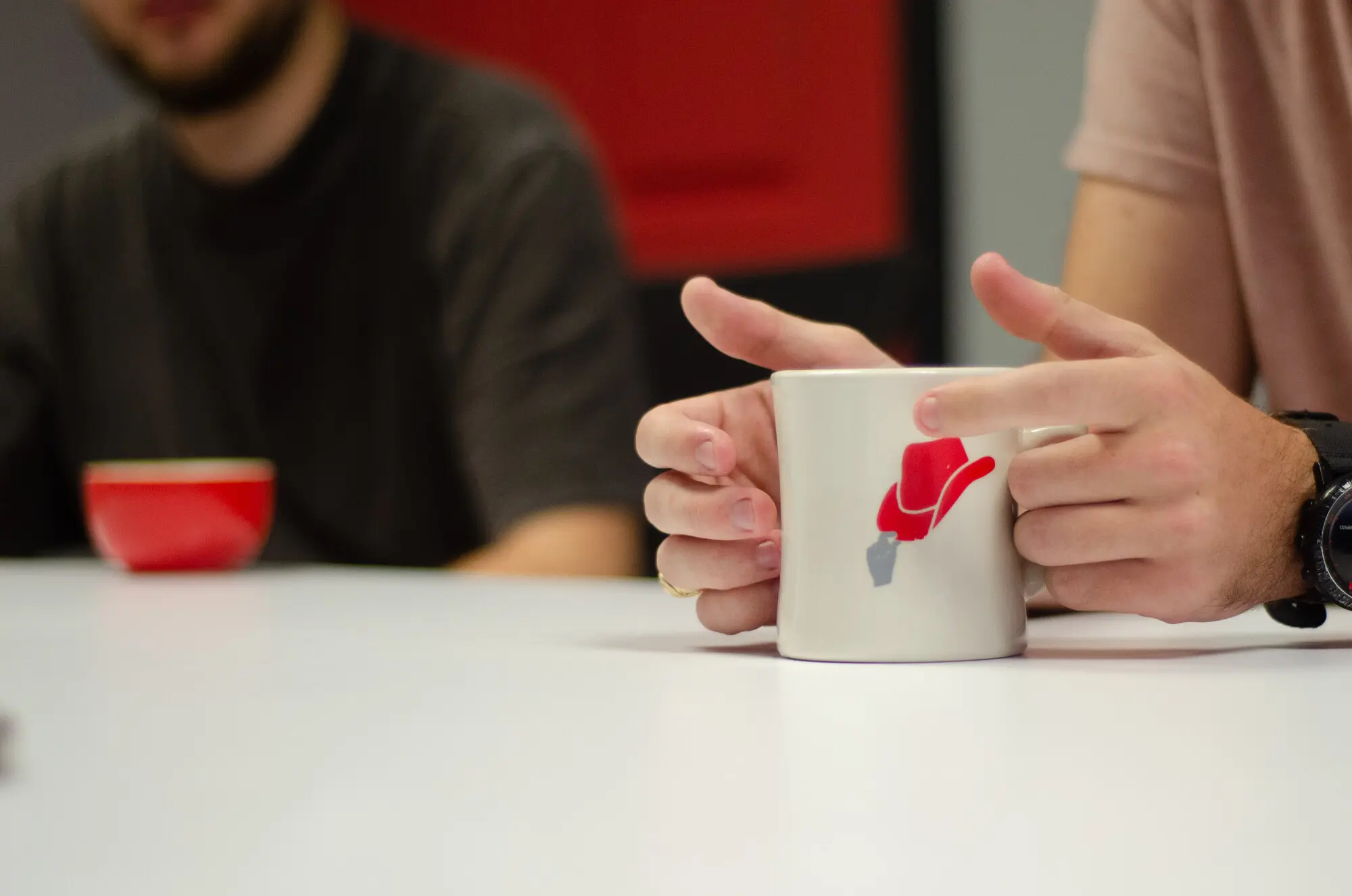 Two QREW team members mid-conversation across a table, hands wrapped around coffee mugs.