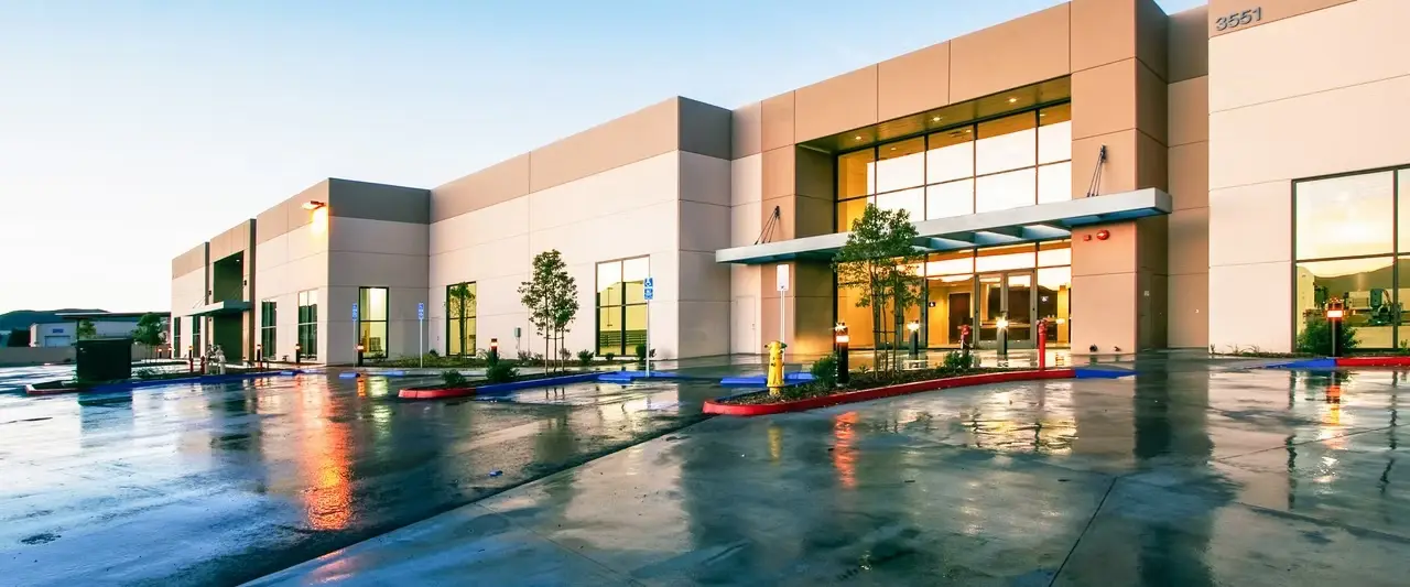 RAMKO Injection's facility at dusk, its glass entrance lit and reflected in the wet forecourt.