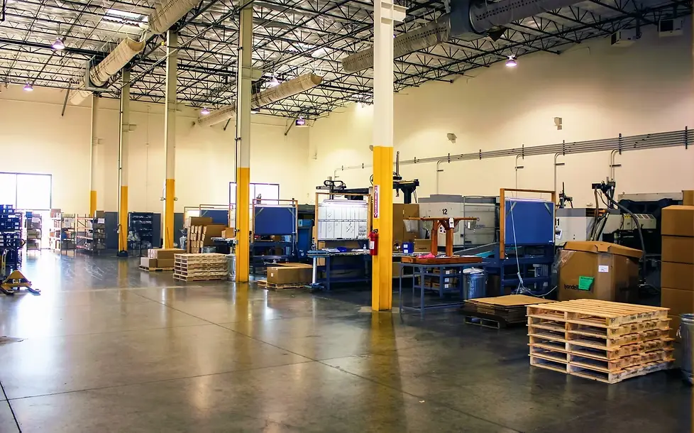 RAMKO Injection's production floor: moulding presses along the far wall, work benches, and stacked pallets under high-bay lighting.